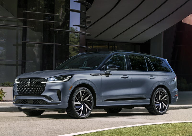 A gray 2025 Lincoln Aviator® SUV is parked outside a modern building showcasing the driver’s side of the vehicle. | Ted Britt Chantilly Lincoln in Chantilly VA