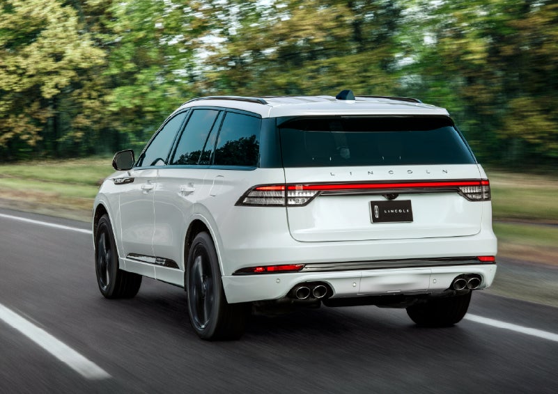 A white 2026 Lincoln Aviator® SUV is being driven away down a road lined with colorful trees. | Ted Britt Chantilly Lincoln in Chantilly VA