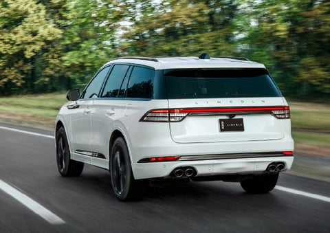 A white 2026 Lincoln Aviator® SUV is being driven away down a road lined with colorful trees. | Ted Britt Chantilly Lincoln in Chantilly VA