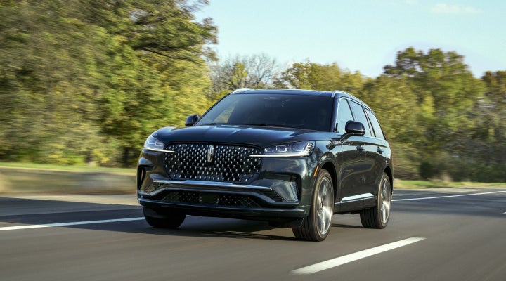 A 2026 Lincoln Black Label™ Aviator® SUV is being driven down a road lined with trees. | Ted Britt Chantilly Lincoln in Chantilly VA