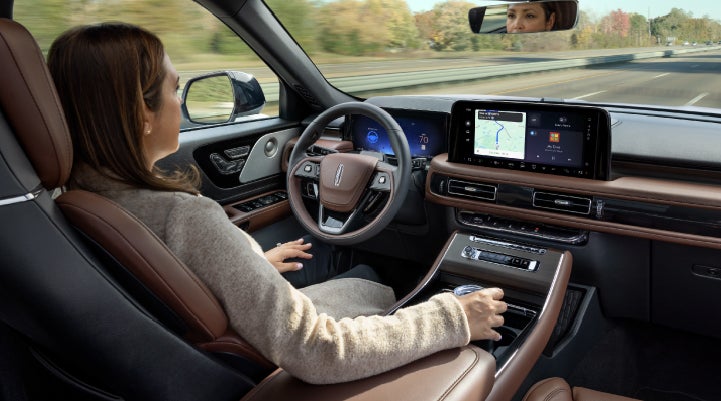 A 2027 Lincoln Aviator® SUV is being driven hands-free on a highway lined with trees. | Ted Britt Chantilly Lincoln in Chantilly VA