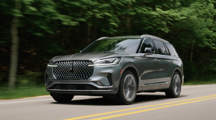 A 2027 Lincoln Aviator® SUV is being driven down a road lined with trees. | Ted Britt Chantilly Lincoln in Chantilly VA