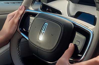 A woman holding the steering wheel inside a Lincoln vehicle.